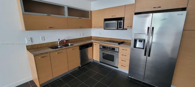 kitchen with appliances with stainless steel finishes, stone countertops, sink, dark tile patterned floors, and light brown cabinets