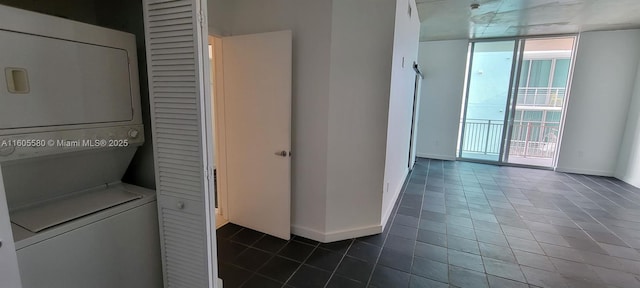 clothes washing area featuring stacked washer and dryer and dark tile patterned flooring