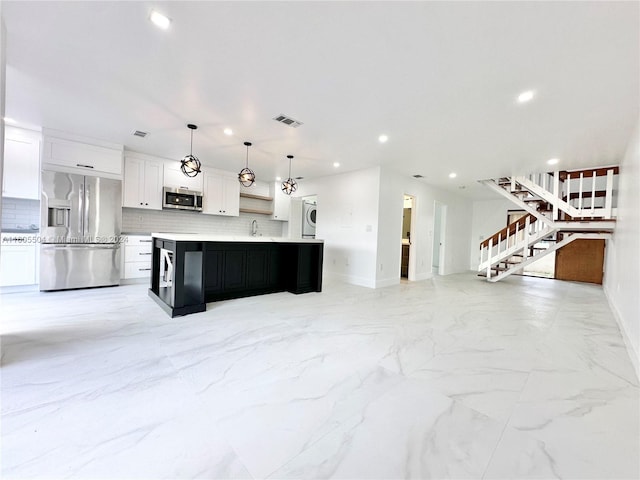 kitchen featuring a large island with sink, white cabinets, hanging light fixtures, decorative backsplash, and appliances with stainless steel finishes