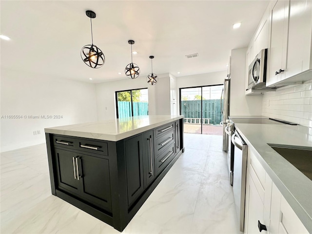 kitchen with hanging light fixtures, white cabinets, backsplash, a kitchen island, and appliances with stainless steel finishes