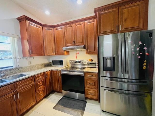 kitchen featuring light stone countertops, sink, light tile floors, and appliances with stainless steel finishes