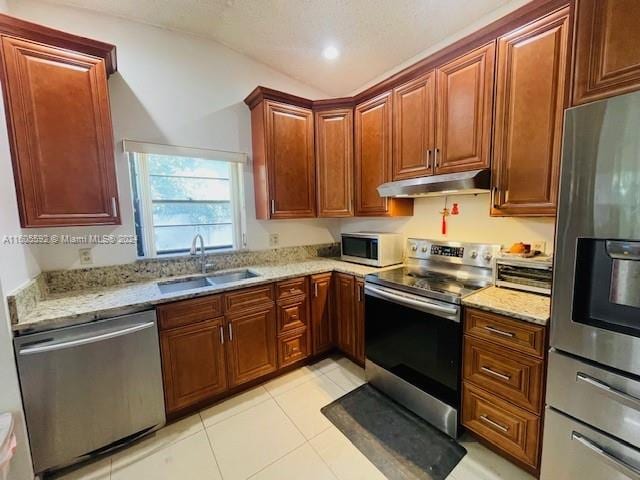 kitchen featuring lofted ceiling, stainless steel appliances, light stone counters, sink, and light tile floors