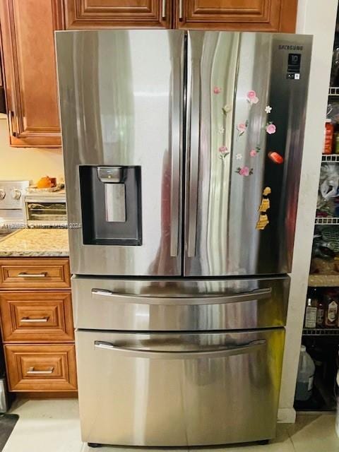 kitchen with light stone countertops, stainless steel fridge with ice dispenser, light tile floors, and range