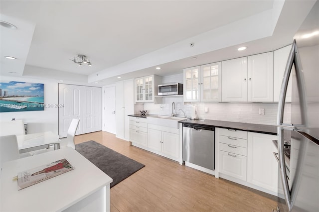 kitchen with decorative backsplash, appliances with stainless steel finishes, sink, light hardwood / wood-style floors, and white cabinetry