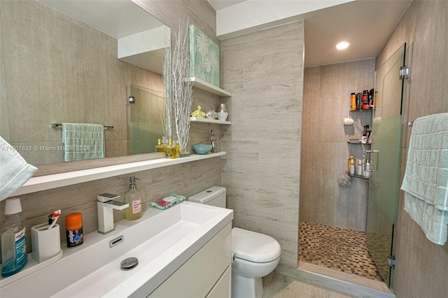 bathroom with tiled shower, vanity, toilet, and tile walls