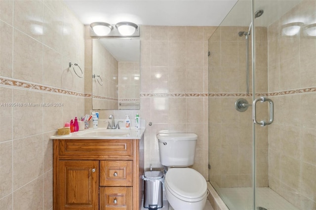 bathroom with a shower with shower door, vanity, toilet, and tile walls