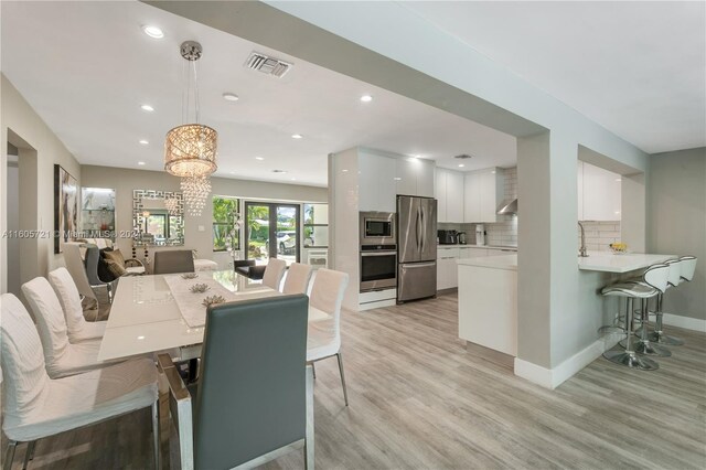 dining room with sink, a notable chandelier, french doors, and light hardwood / wood-style floors