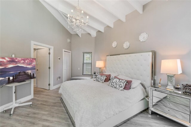 bedroom with a closet, light hardwood / wood-style floors, a notable chandelier, and vaulted ceiling with beams