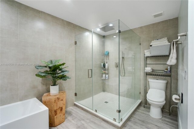 bathroom featuring hardwood / wood-style floors, tile walls, toilet, and independent shower and bath