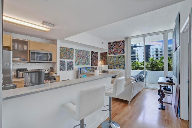 interior space featuring light brown cabinets, kitchen peninsula, light hardwood / wood-style floors, and appliances with stainless steel finishes