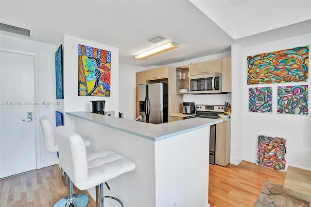 kitchen featuring light hardwood / wood-style flooring, stainless steel appliances, kitchen peninsula, and a breakfast bar area