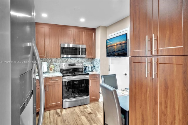 kitchen featuring light wood-type flooring, appliances with stainless steel finishes, decorative backsplash, and light stone countertops