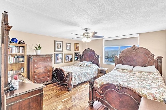 bedroom with a textured ceiling, ceiling fan, and light hardwood / wood-style floors