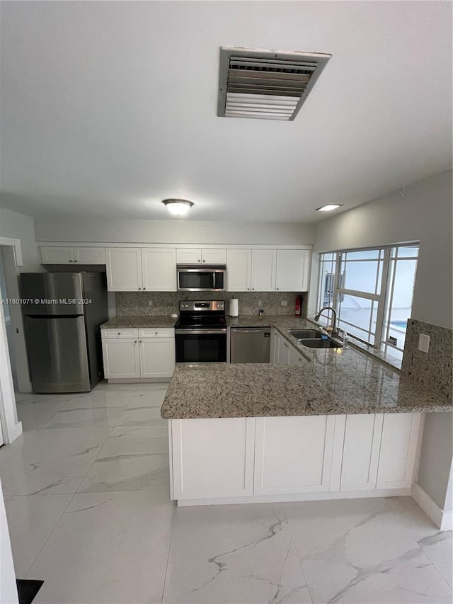 kitchen featuring kitchen peninsula, sink, decorative backsplash, appliances with stainless steel finishes, and white cabinetry