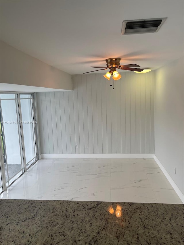 empty room featuring ceiling fan and wood walls