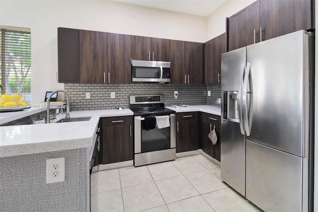 kitchen with appliances with stainless steel finishes, tasteful backsplash, light tile patterned floors, dark brown cabinetry, and light stone countertops