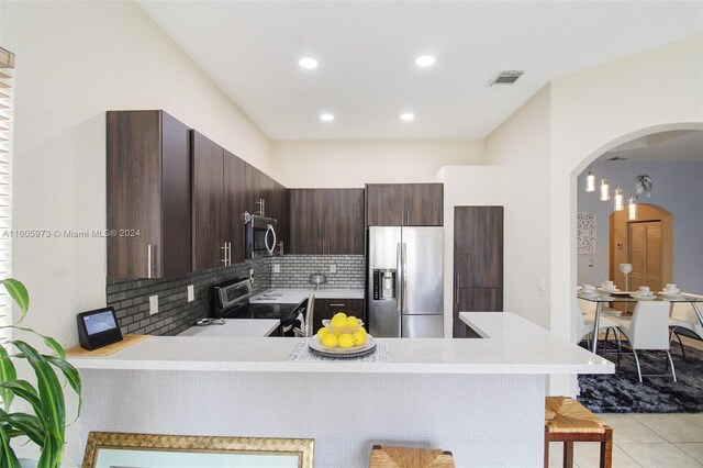 kitchen with light tile patterned flooring, decorative backsplash, a kitchen bar, appliances with stainless steel finishes, and kitchen peninsula