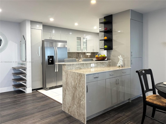 kitchen featuring stainless steel fridge with ice dispenser, light stone countertops, dark hardwood / wood-style flooring, decorative backsplash, and white cabinetry