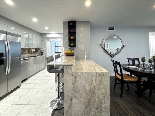 kitchen with stainless steel appliances, kitchen peninsula, sink, white cabinetry, and tasteful backsplash