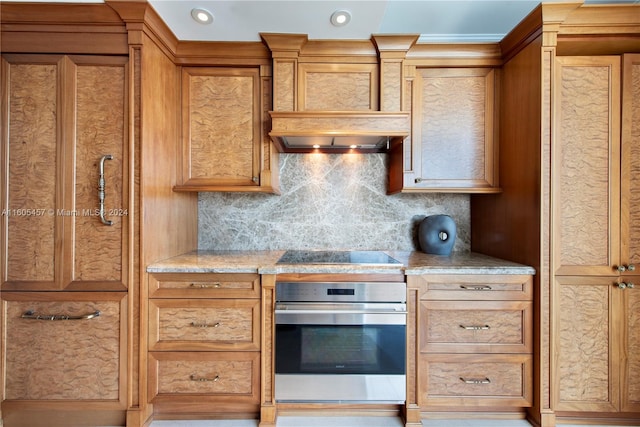 kitchen with stainless steel oven, black electric stovetop, light stone countertops, tasteful backsplash, and custom range hood