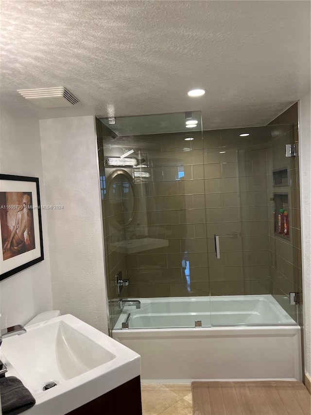 bathroom with tile flooring, combined bath / shower with glass door, vanity, and a textured ceiling