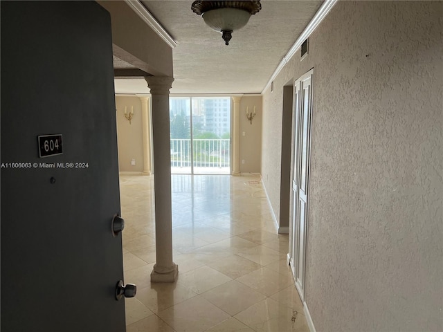 corridor with a textured ceiling, ornate columns, ornamental molding, and a wall of windows