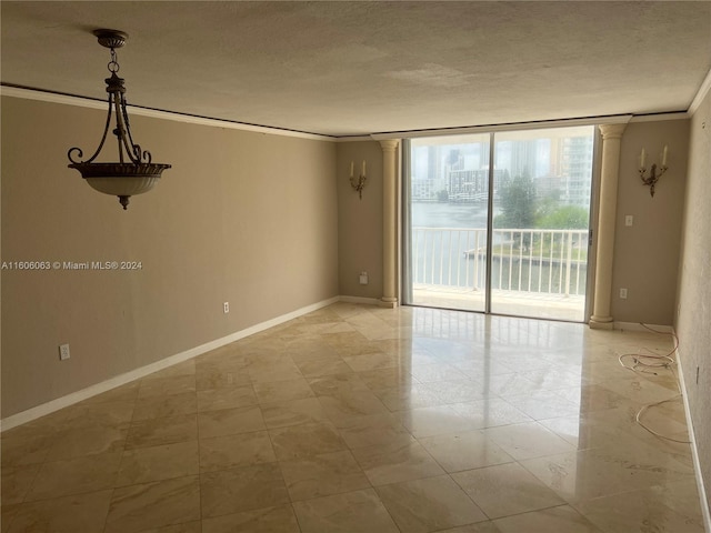 tiled empty room featuring decorative columns, a textured ceiling, expansive windows, and ornamental molding