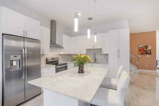 kitchen featuring pendant lighting, wall chimney exhaust hood, appliances with stainless steel finishes, a kitchen island, and white cabinetry