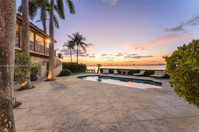 pool at dusk with a water view and a patio