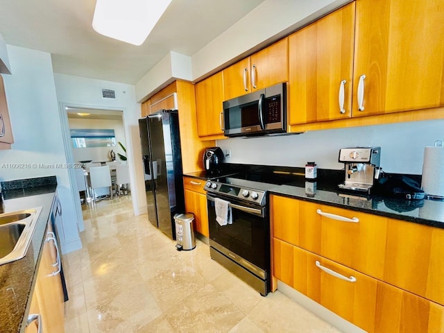 kitchen with appliances with stainless steel finishes, dark stone countertops, and sink