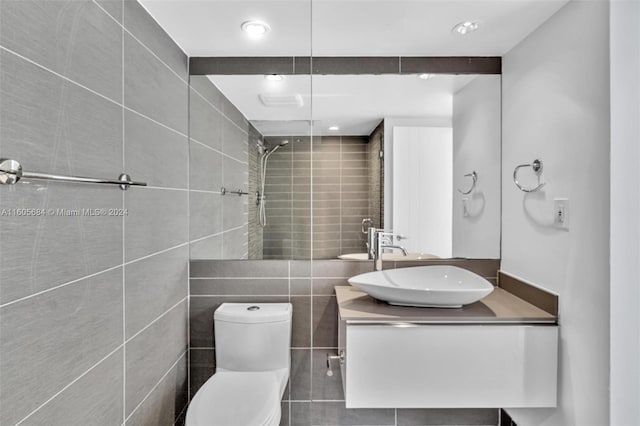 bathroom featuring a tile shower, vanity, tile walls, and toilet