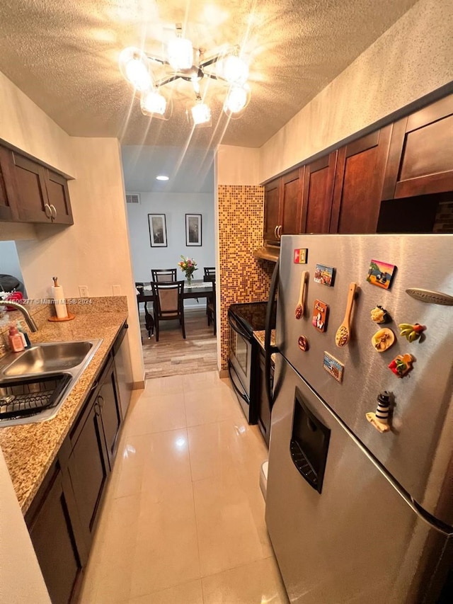 kitchen with appliances with stainless steel finishes, light stone counters, a chandelier, sink, and light tile flooring