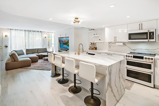 kitchen featuring white cabinetry, backsplash, an island with sink, double oven range, and a breakfast bar area