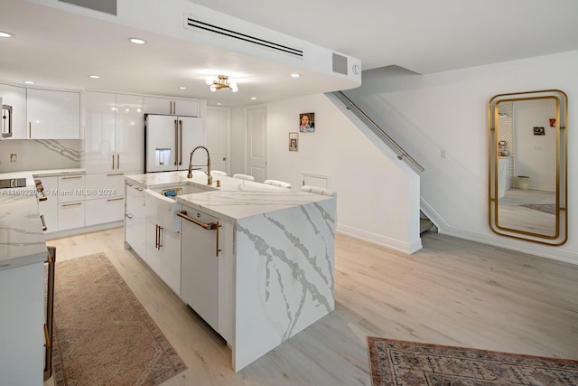 kitchen featuring light stone counters, white cabinets, high end fridge, and an island with sink