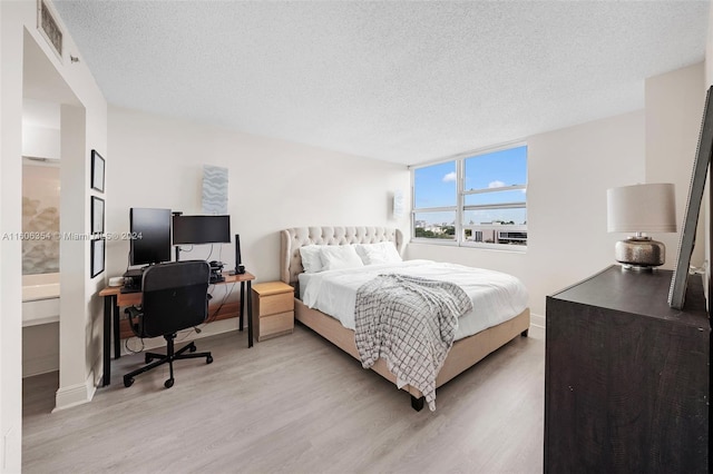 bedroom with ensuite bath, light hardwood / wood-style floors, and a textured ceiling