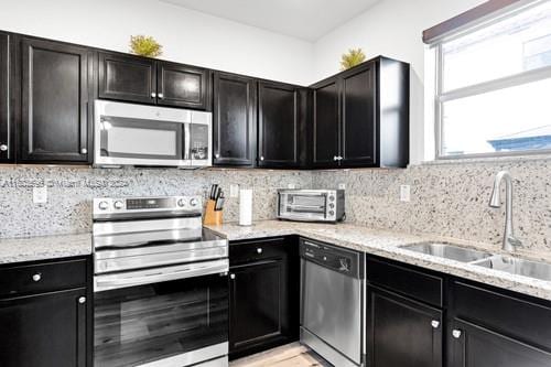 kitchen featuring sink, light stone counters, backsplash, and appliances with stainless steel finishes