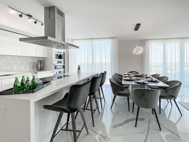 kitchen with a wealth of natural light, white cabinetry, stovetop, backsplash, and island exhaust hood