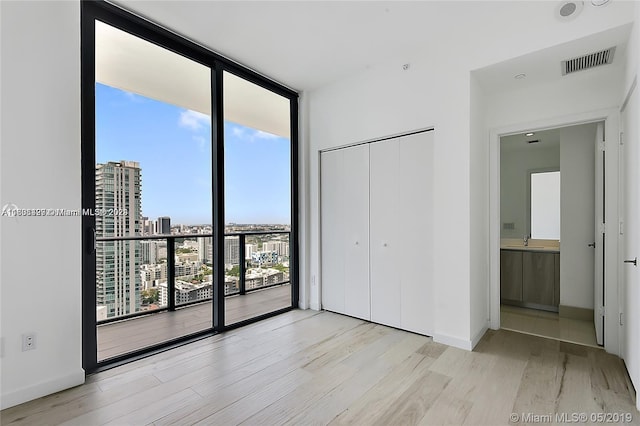 unfurnished bedroom with a closet, light hardwood / wood-style flooring, floor to ceiling windows, sink, and connected bathroom