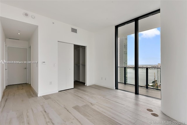 unfurnished bedroom featuring expansive windows, a closet, and light wood-type flooring