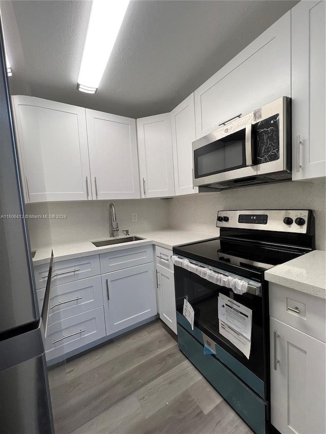 kitchen featuring white cabinetry, light wood-type flooring, sink, light stone counters, and appliances with stainless steel finishes