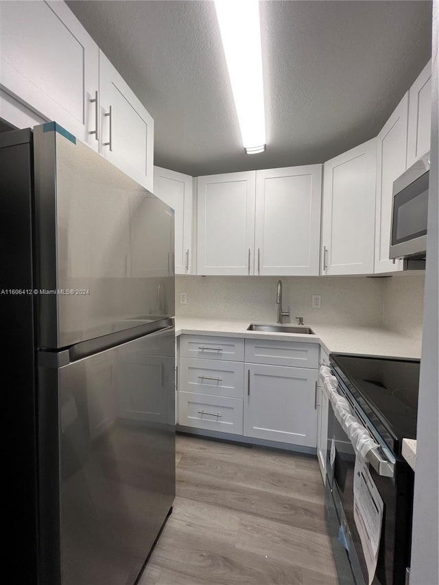 kitchen with stainless steel appliances, sink, white cabinets, and light hardwood / wood-style flooring