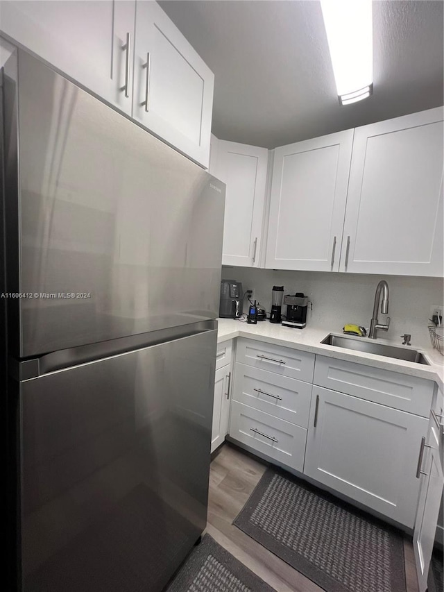 kitchen with white cabinetry, sink, stainless steel fridge, and wood-type flooring