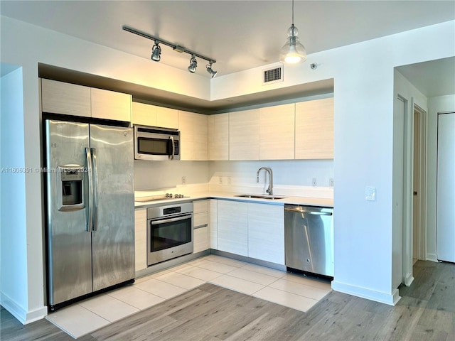 kitchen with rail lighting, stainless steel appliances, sink, light hardwood / wood-style floors, and decorative light fixtures