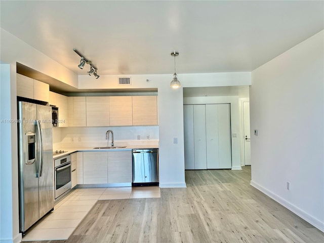 kitchen with appliances with stainless steel finishes, sink, hanging light fixtures, light hardwood / wood-style floors, and track lighting