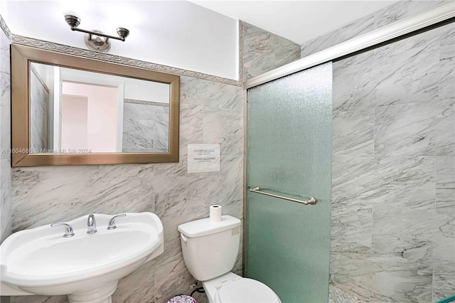 bathroom with a shower with door, sink, toilet, and tile walls