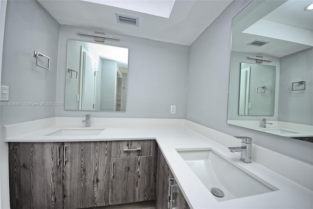 bathroom featuring a skylight, oversized vanity, and double sink