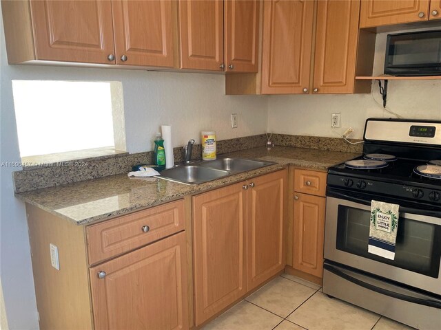 kitchen featuring light stone countertops, sink, stainless steel range with gas stovetop, and light tile floors