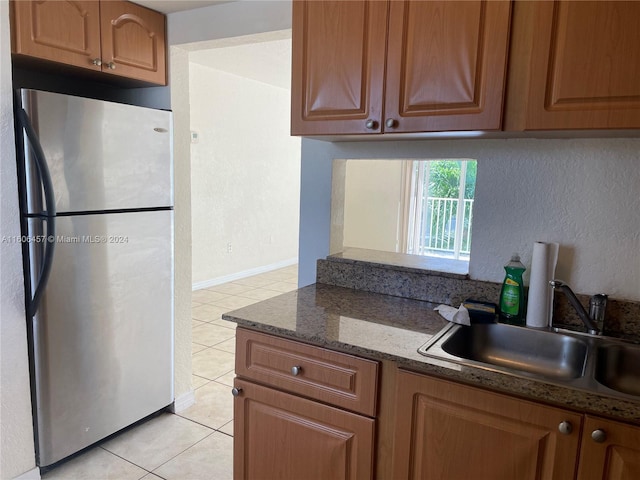 kitchen with dark stone counters, sink, stainless steel fridge, and light tile flooring