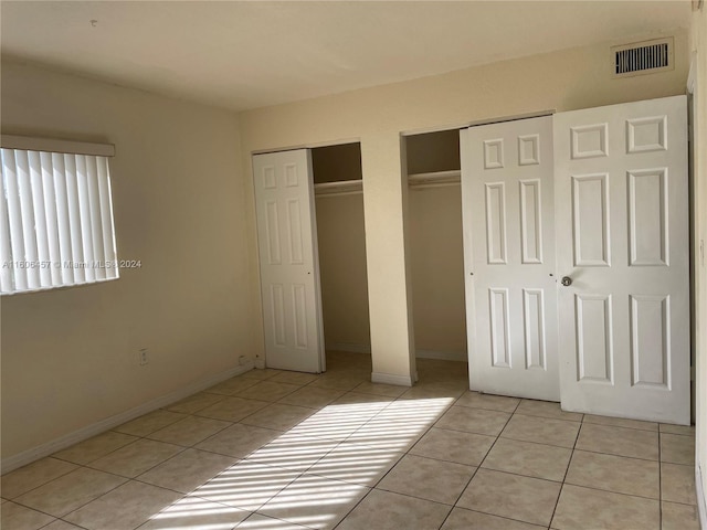 unfurnished bedroom with multiple closets and light tile floors