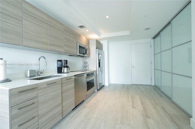 kitchen with sink, appliances with stainless steel finishes, and light hardwood / wood-style flooring